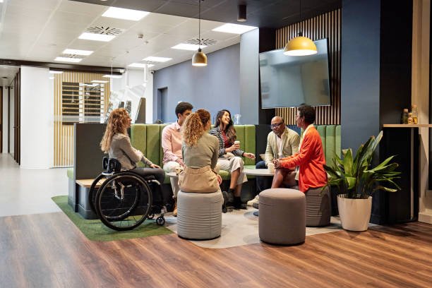 Diverse group of professionals, including a woman using a wheelchair, sitting in a circle and having a discussion in a modern, inclusive office space.