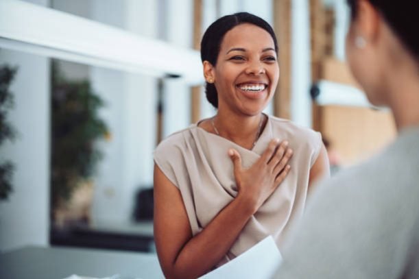 A woman smiles warmly with her hand on her chest, expressing gratitude and happiness during a heartfelt conversation.