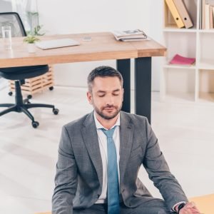 handsome businessman meditating in Lotus Pose on fitness mat in office